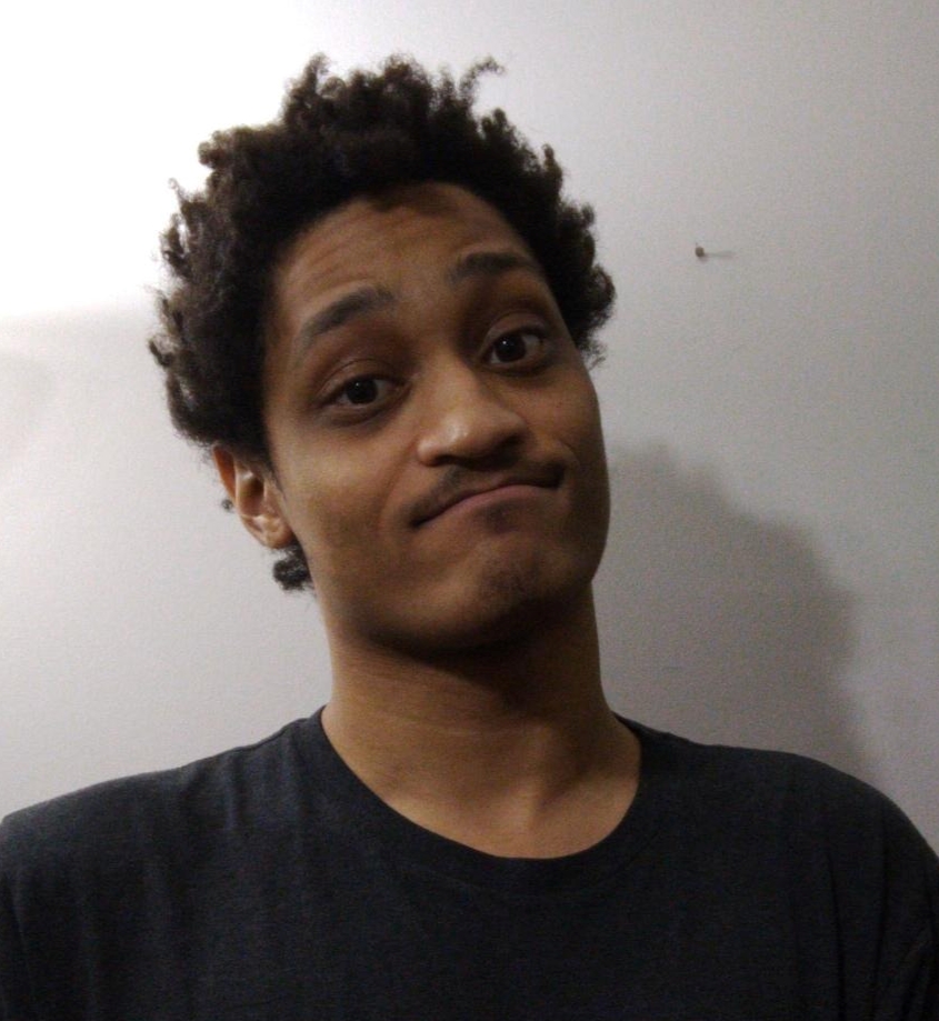 A photograph of Aaron, a man with tan skin and black hair wearing a black shirt